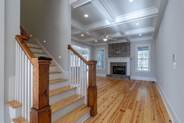 staircase with ceiling fan, coffered ceiling, beamed ceiling, wood-type flooring, and a fireplace