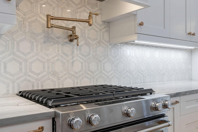 kitchen with stainless steel range, backsplash, white cabinetry, and light stone countertops