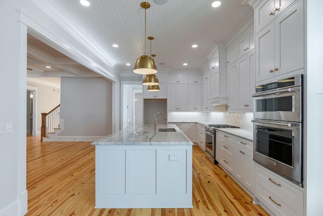 kitchen with stainless steel appliances, a kitchen island with sink, sink, decorative light fixtures, and white cabinets