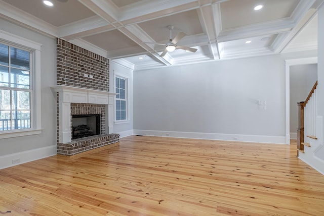 unfurnished living room featuring a brick fireplace, coffered ceiling, crown molding, beam ceiling, and light hardwood / wood-style flooring