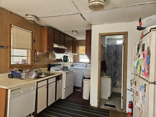 kitchen with washing machine and clothes dryer, wood walls, sink, and white appliances