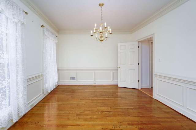 empty room with wood-type flooring, ornamental molding, and a chandelier