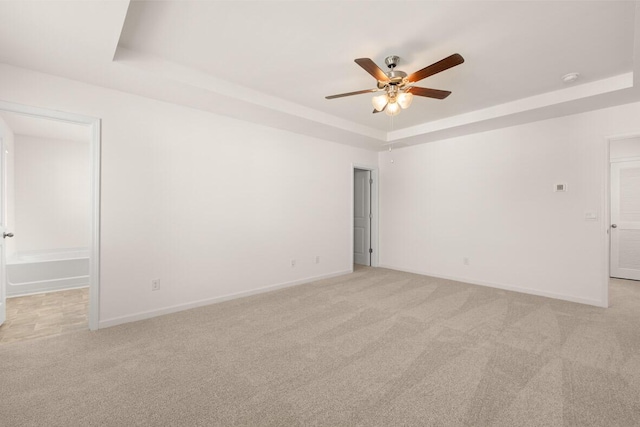 empty room with light carpet, ceiling fan, and a tray ceiling