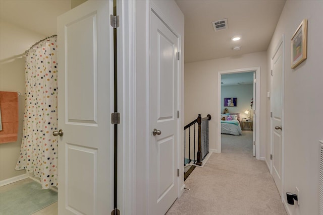 hall featuring visible vents, baseboards, and light carpet