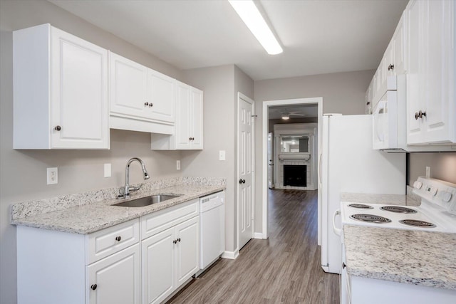 kitchen featuring a sink, white cabinetry, white appliances, light wood finished floors, and a brick fireplace