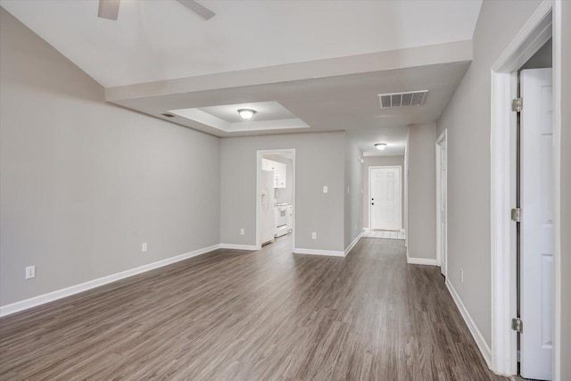 spare room featuring baseboards, visible vents, a tray ceiling, ceiling fan, and dark wood-type flooring