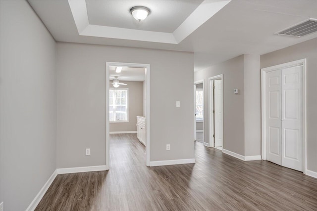 spare room featuring visible vents, a raised ceiling, baseboards, and wood finished floors