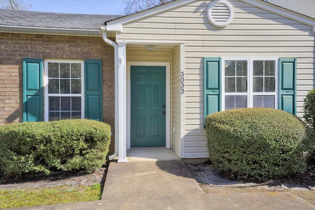 entrance to property featuring brick siding and roof with shingles