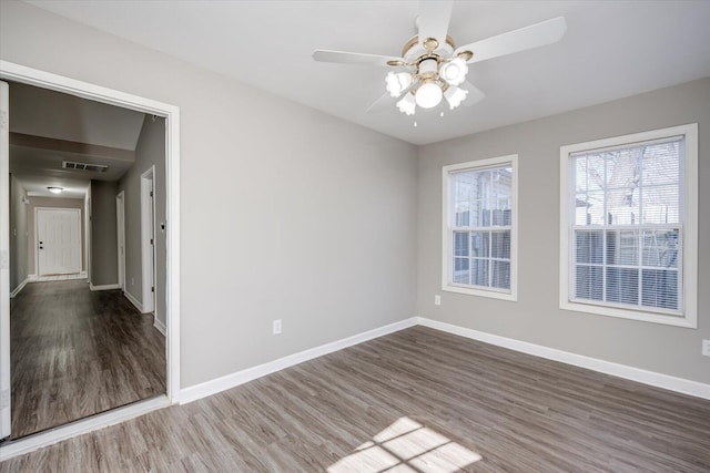 empty room featuring ceiling fan, visible vents, baseboards, and wood finished floors