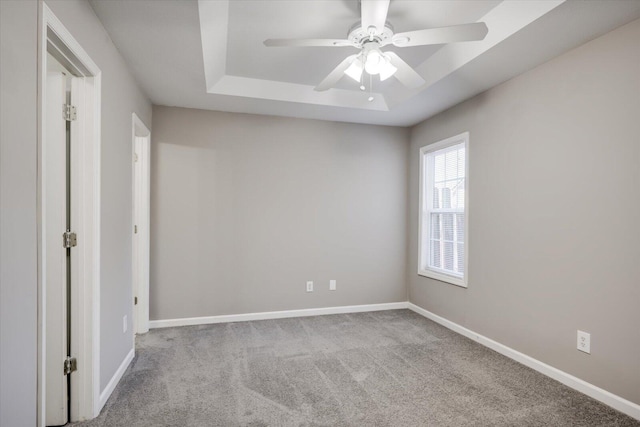 spare room featuring a tray ceiling, carpet flooring, a ceiling fan, and baseboards