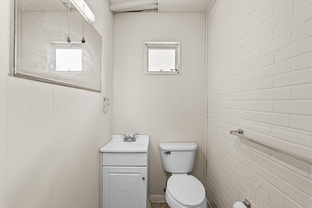 half bath featuring toilet, brick wall, and vanity