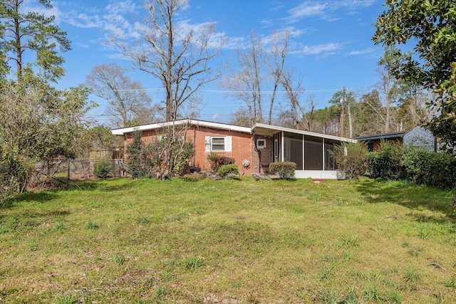 rear view of property featuring a sunroom, brick siding, a lawn, and fence