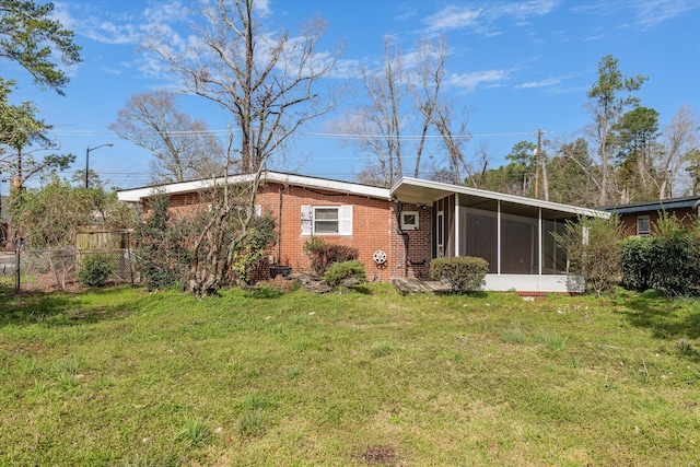 rear view of house with a sunroom, brick siding, a lawn, and fence