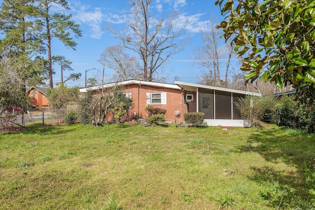 back of house featuring a sunroom, fence, a lawn, and brick siding