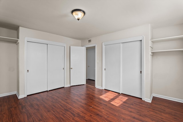 unfurnished bedroom with wood finished floors, two closets, visible vents, and baseboards