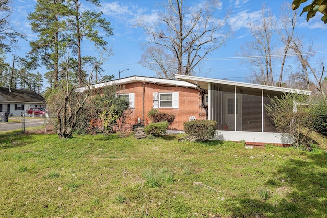 rear view of house featuring brick siding, a lawn, fence, and a sunroom