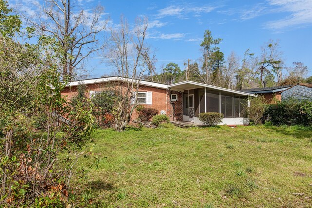 rear view of property with a sunroom, brick siding, and a yard