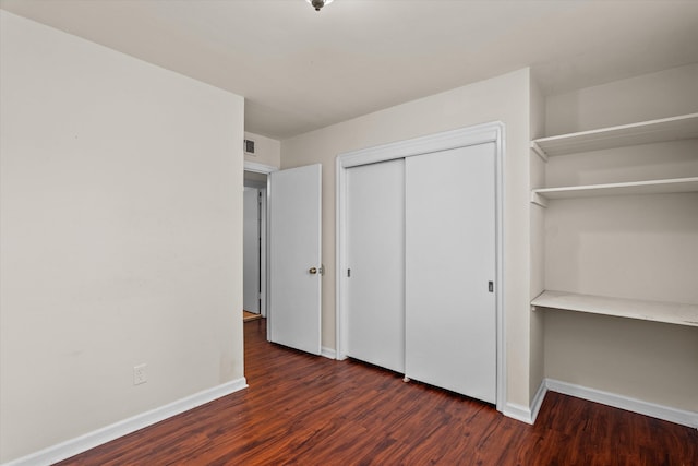 unfurnished bedroom featuring visible vents, a closet, baseboards, and dark wood-style flooring