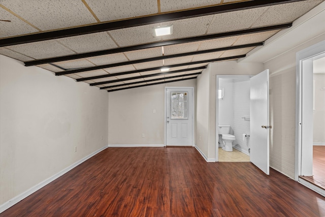 empty room with baseboards, wood finished floors, and beamed ceiling