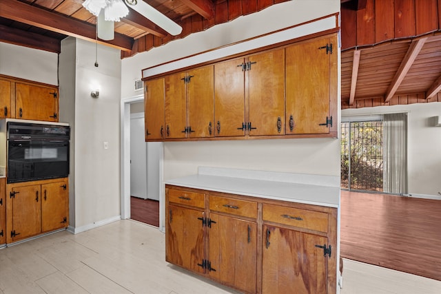 kitchen with brown cabinetry, wood ceiling, light countertops, beam ceiling, and black oven