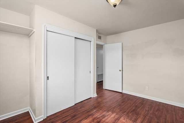 unfurnished bedroom with dark wood-type flooring, a closet, visible vents, and baseboards