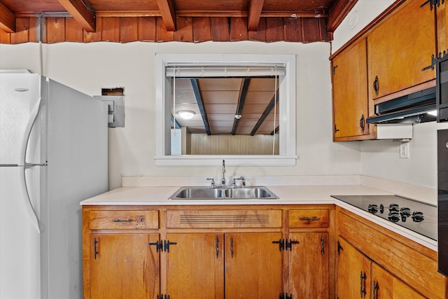 kitchen with brown cabinetry, freestanding refrigerator, black electric stovetop, light countertops, and a sink