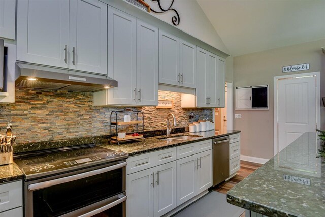 kitchen with backsplash, stainless steel appliances, vaulted ceiling, sink, and dark stone countertops