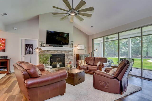 living room with a stone fireplace, ceiling fan, light hardwood / wood-style floors, and vaulted ceiling