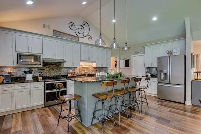 1370 Deerwood Cir, Stapleton, GA 30823 - kitchen featuring appliances with stainless steel finishes, under cabinet range hood, a breakfast bar area, high vaulted ceiling, and a kitchen island