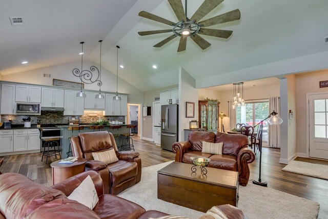 living room featuring ceiling fan with notable chandelier, high vaulted ceiling, and dark wood-type flooring