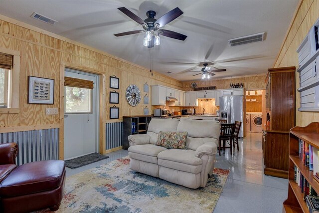 living room with sink, ceiling fan, wood walls, and washing machine and clothes dryer