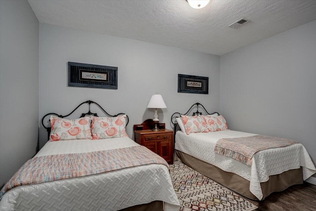 bedroom with visible vents, a textured ceiling, and wood finished floors