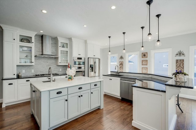 kitchen with dark wood-type flooring, wall chimney range hood, appliances with stainless steel finishes, a large island, and a sink