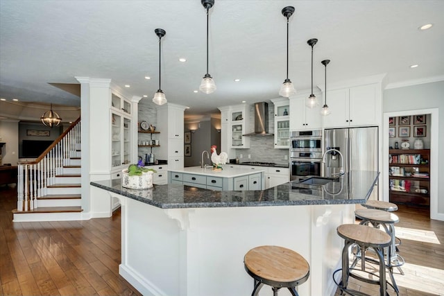 kitchen with a sink, appliances with stainless steel finishes, crown molding, wall chimney range hood, and a large island with sink