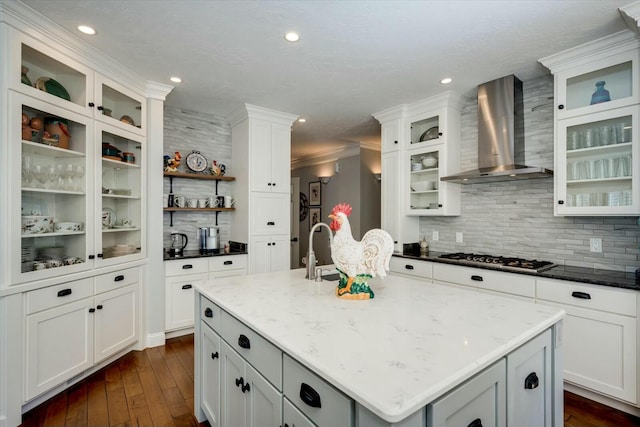 kitchen with dark wood finished floors, an island with sink, stainless steel gas stovetop, wall chimney exhaust hood, and a sink