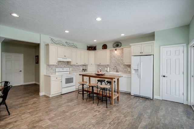 kitchen featuring light wood-type flooring, under cabinet range hood, a sink, tasteful backsplash, and white appliances