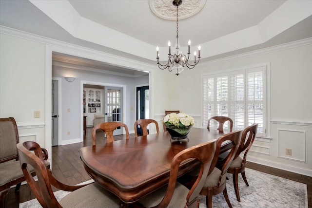 dining area featuring a chandelier, a decorative wall, a raised ceiling, and dark wood-style flooring