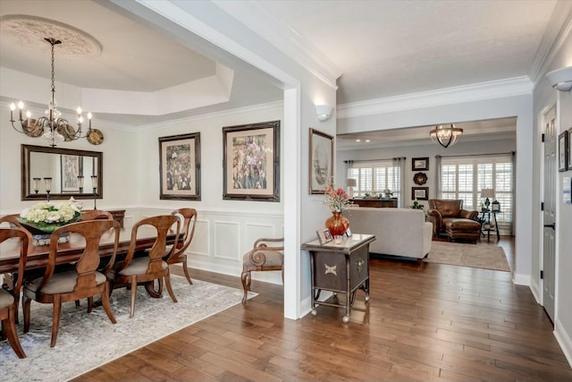 dining area featuring an inviting chandelier, a tray ceiling, dark wood-style flooring, ornamental molding, and a decorative wall