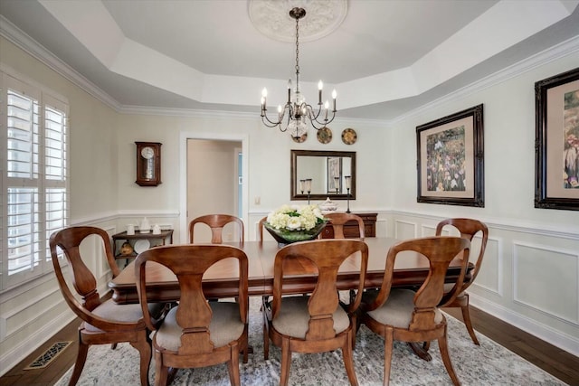 dining area featuring a tray ceiling, wood finished floors, visible vents, and a chandelier