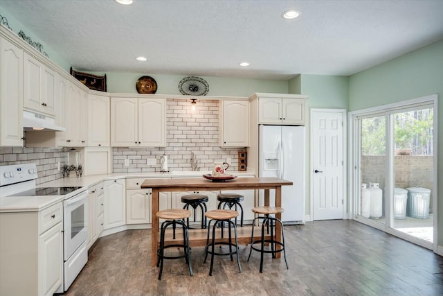 kitchen with under cabinet range hood, tasteful backsplash, wood finished floors, recessed lighting, and white appliances