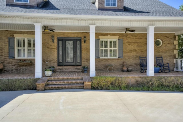 entrance to property with brick siding, covered porch, a ceiling fan, and roof with shingles