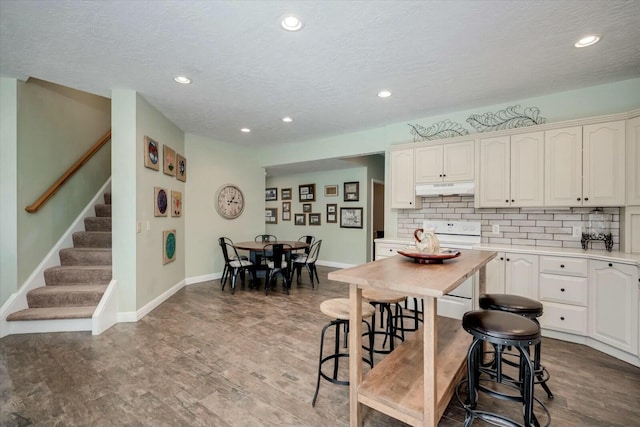 kitchen featuring white electric range oven, baseboards, light countertops, under cabinet range hood, and tasteful backsplash