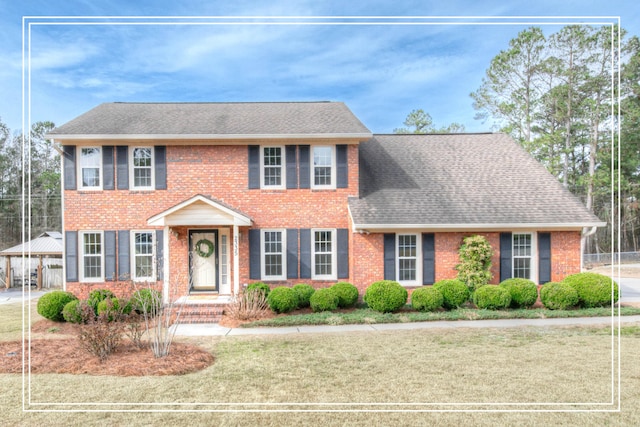 colonial home featuring brick siding, a front lawn, and roof with shingles