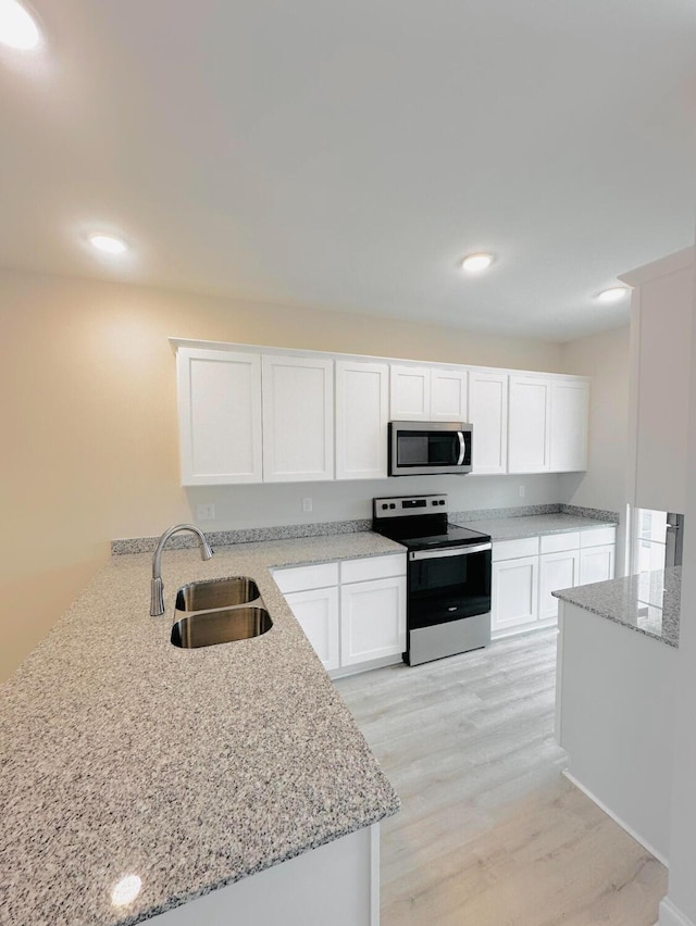 kitchen with white cabinets, sink, light stone counters, kitchen peninsula, and stainless steel appliances