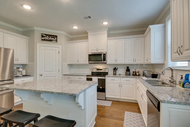3120 Wayne Dr, Evans, GA 30809 - kitchen with appliances with stainless steel finishes, a sink, a kitchen breakfast bar, white cabinetry, and ornamental molding