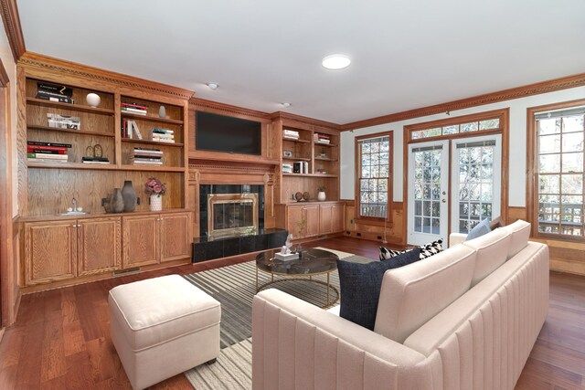 living room with a tiled fireplace, crown molding, dark hardwood / wood-style flooring, and built in features