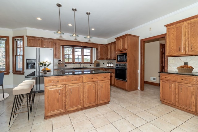 kitchen with dark stone counters, a kitchen island, hanging light fixtures, and black appliances