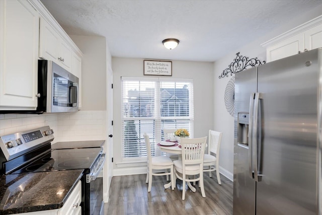 kitchen with dark wood-type flooring, dark stone countertops, backsplash, stainless steel appliances, and white cabinets