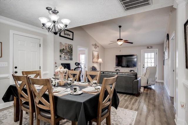 dining space with ceiling fan with notable chandelier, a fireplace, lofted ceiling, hardwood / wood-style flooring, and a textured ceiling