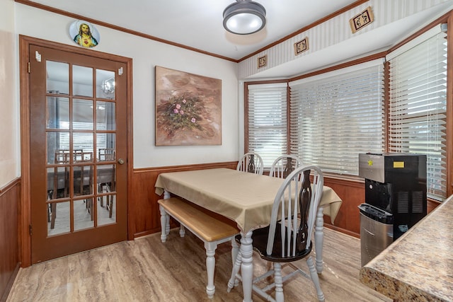 dining room with a wainscoted wall, light wood-style floors, ornamental molding, and wooden walls